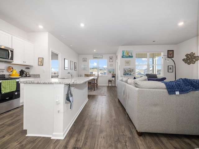 kitchen featuring appliances with stainless steel finishes, a kitchen breakfast bar, a center island with sink, dark hardwood / wood-style floors, and white cabinetry