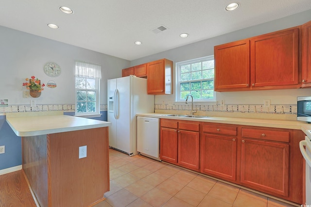 kitchen with kitchen peninsula, white appliances, plenty of natural light, and sink