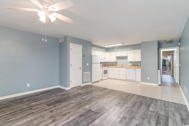 kitchen featuring white appliances, sink, a textured ceiling, light hardwood / wood-style floors, and white cabinetry