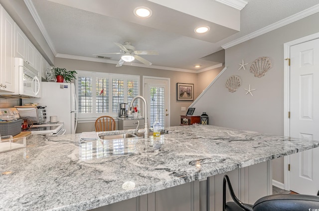 kitchen featuring white appliances, sink, ceiling fan, light stone counters, and white cabinetry