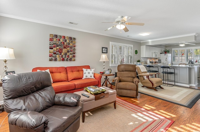 living room with ceiling fan, light hardwood / wood-style flooring, a textured ceiling, and ornamental molding