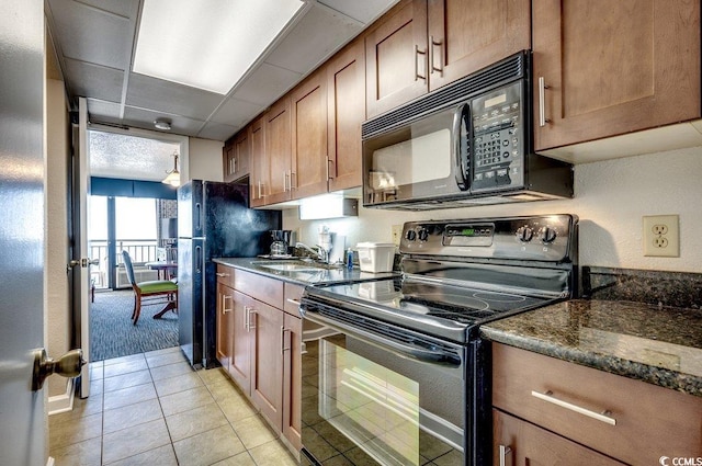 kitchen with a drop ceiling, dark stone counters, black appliances, sink, and light tile patterned floors