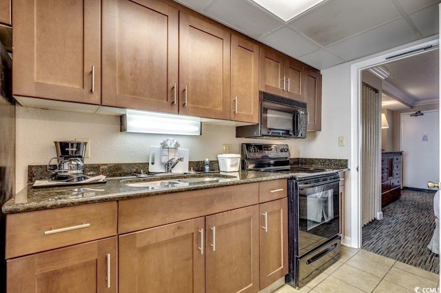 kitchen featuring a paneled ceiling, black appliances, sink, dark stone countertops, and light tile patterned floors