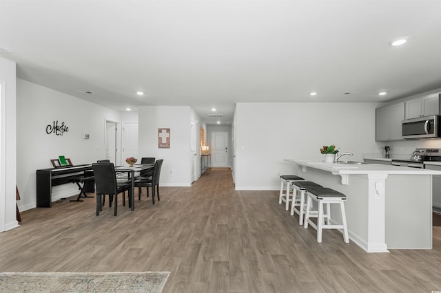 kitchen featuring appliances with stainless steel finishes, a kitchen breakfast bar, light hardwood / wood-style flooring, gray cabinets, and an island with sink