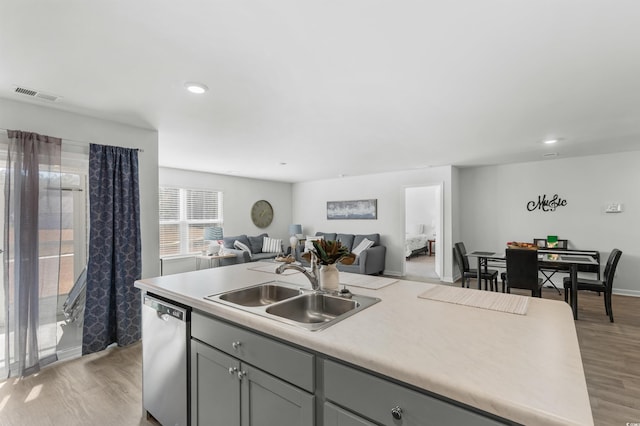 kitchen featuring a kitchen island with sink, sink, light hardwood / wood-style flooring, stainless steel dishwasher, and gray cabinets