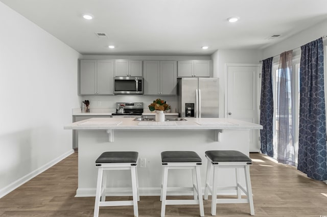 kitchen featuring gray cabinetry, light wood-type flooring, a kitchen island with sink, and appliances with stainless steel finishes