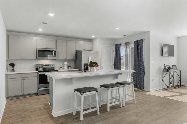 kitchen featuring an island with sink, light hardwood / wood-style floors, a breakfast bar area, gray cabinets, and appliances with stainless steel finishes