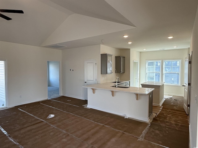 kitchen featuring a kitchen bar, a peninsula, light countertops, ceiling fan, and vaulted ceiling