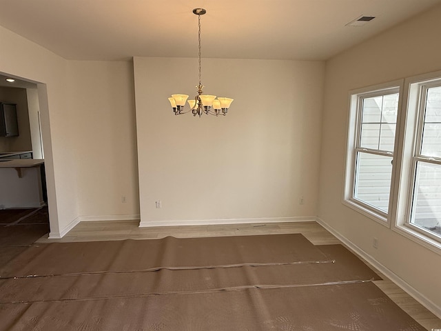 unfurnished dining area with visible vents, baseboards, an inviting chandelier, and wood finished floors