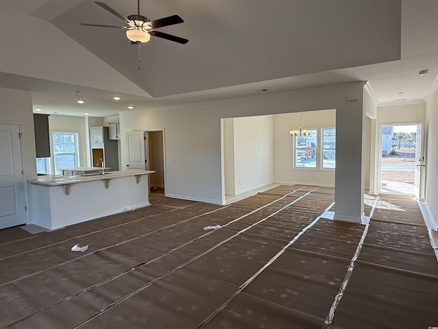 unfurnished living room with baseboards, ornamental molding, ceiling fan with notable chandelier, high vaulted ceiling, and a sink