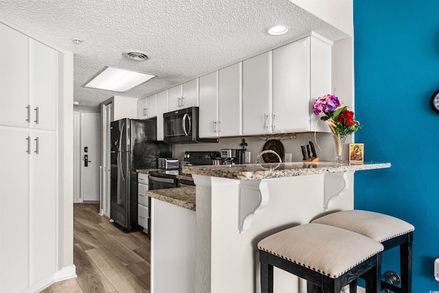 kitchen with white cabinetry, dark stone countertops, a kitchen breakfast bar, black appliances, and kitchen peninsula