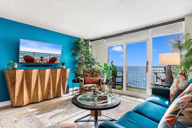 living room with a water view, floor to ceiling windows, a textured ceiling, and light wood-type flooring