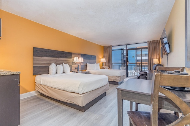 bedroom with a textured ceiling, access to outside, light hardwood / wood-style flooring, and a wall of windows