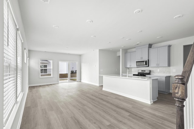 kitchen with gray cabinetry, a kitchen island with sink, light hardwood / wood-style floors, decorative backsplash, and stainless steel appliances