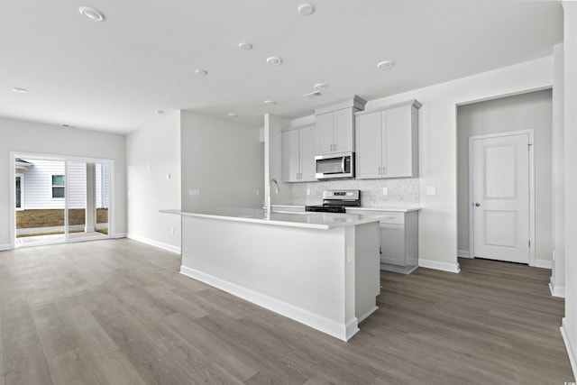 kitchen with hardwood / wood-style floors, tasteful backsplash, sink, stainless steel appliances, and a center island with sink