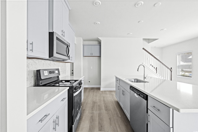 kitchen with light hardwood / wood-style flooring, sink, a kitchen island with sink, decorative backsplash, and stainless steel appliances