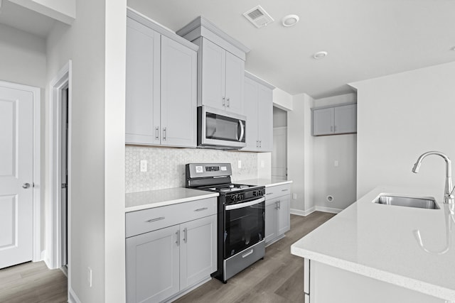 kitchen featuring stainless steel appliances, decorative backsplash, sink, hardwood / wood-style flooring, and gray cabinetry