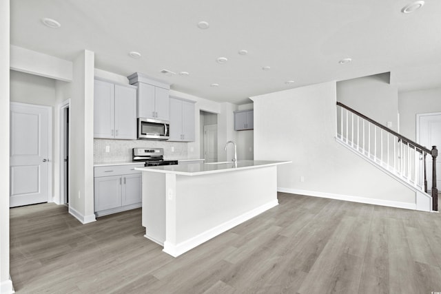 kitchen featuring stainless steel appliances, light hardwood / wood-style floors, decorative backsplash, and an island with sink