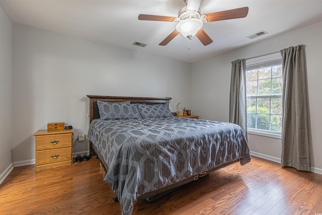 bedroom with a ceiling fan, baseboards, visible vents, and wood finished floors