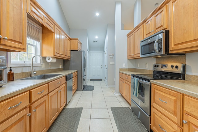 kitchen featuring light tile patterned floors, stainless steel appliances, a sink, baseboards, and light countertops