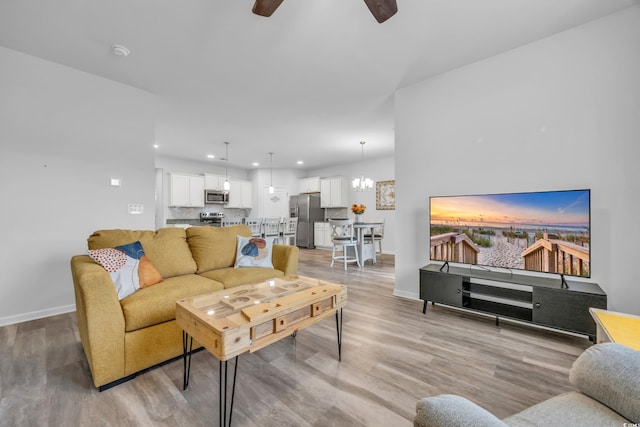 living room featuring ceiling fan with notable chandelier and light hardwood / wood-style floors