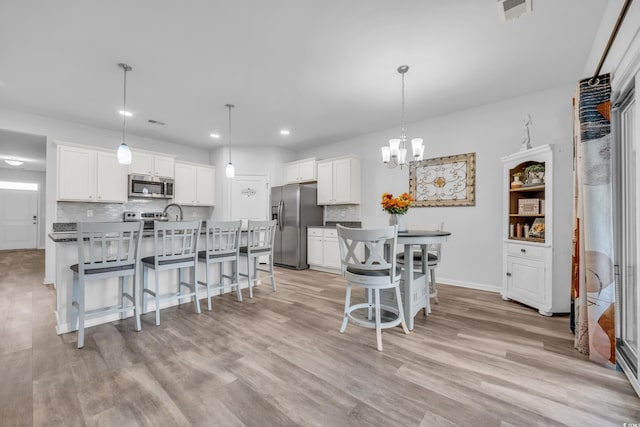 kitchen with a breakfast bar, pendant lighting, white cabinets, and stainless steel appliances