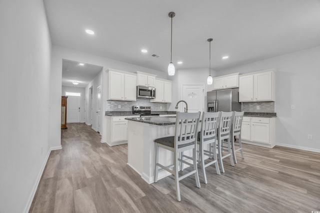 kitchen with a center island with sink, white cabinetry, stainless steel appliances, and light hardwood / wood-style flooring