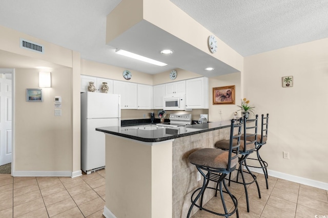 kitchen with white appliances, kitchen peninsula, light tile patterned floors, a kitchen bar, and white cabinetry