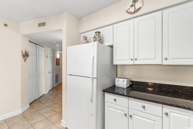 kitchen with white fridge, light tile patterned flooring, white cabinetry, and dark stone counters