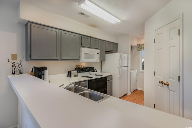 kitchen featuring sink, light hardwood / wood-style floors, white appliances, washer / dryer, and gray cabinets