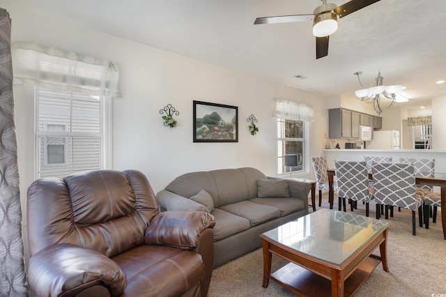 carpeted living room with ceiling fan with notable chandelier