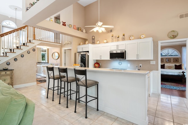 kitchen featuring a breakfast bar, white cabinets, a towering ceiling, appliances with stainless steel finishes, and a kitchen island