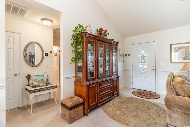 foyer featuring light carpet, a textured ceiling, and vaulted ceiling