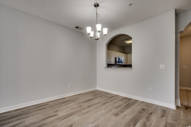 empty room with light hardwood / wood-style flooring, a textured ceiling, and an inviting chandelier