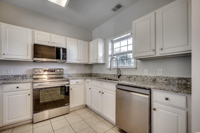 kitchen with light stone counters, stainless steel appliances, sink, light tile patterned floors, and white cabinets