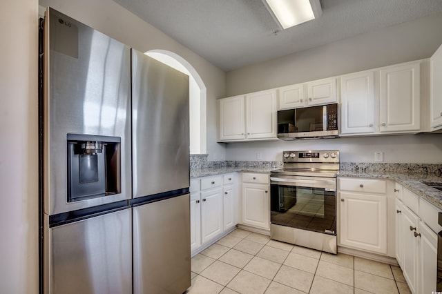 kitchen with light stone countertops, white cabinetry, stainless steel appliances, and light tile patterned floors