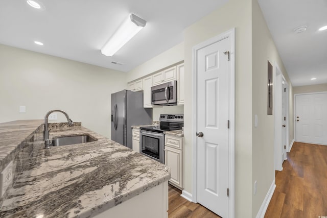 kitchen featuring light stone countertops, appliances with stainless steel finishes, wood-type flooring, white cabinetry, and sink