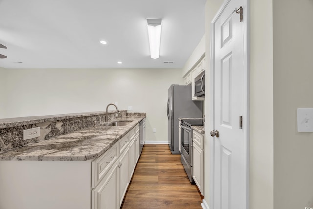 kitchen featuring hardwood / wood-style floors, sink, white cabinetry, light stone countertops, and appliances with stainless steel finishes