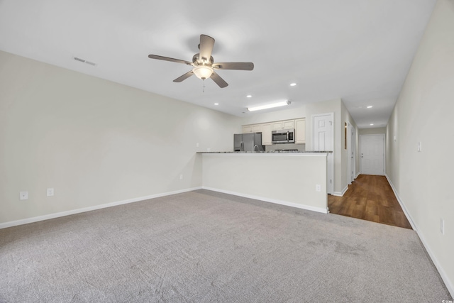 unfurnished living room featuring ceiling fan and dark carpet