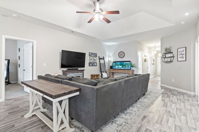 living room with ceiling fan, a raised ceiling, and light hardwood / wood-style flooring