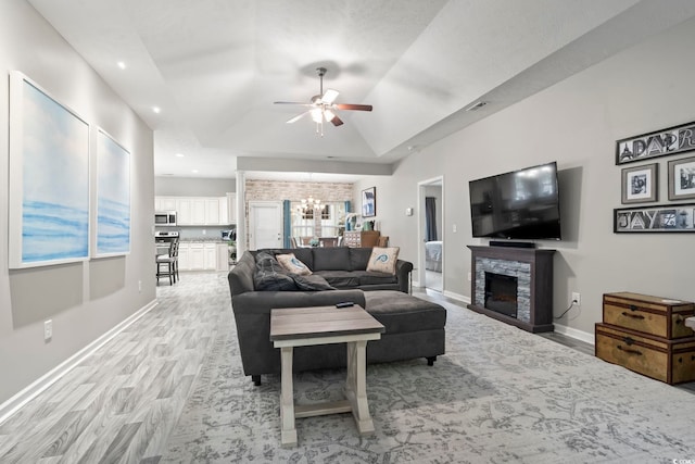 living room featuring ceiling fan with notable chandelier, a fireplace, lofted ceiling, light hardwood / wood-style floors, and a raised ceiling