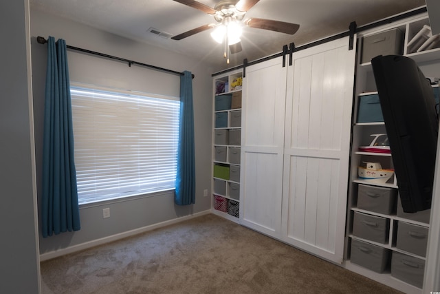 unfurnished bedroom with carpet floors, a barn door, and ceiling fan