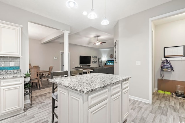 kitchen featuring ornate columns, a kitchen island, white cabinetry, backsplash, and ceiling fan