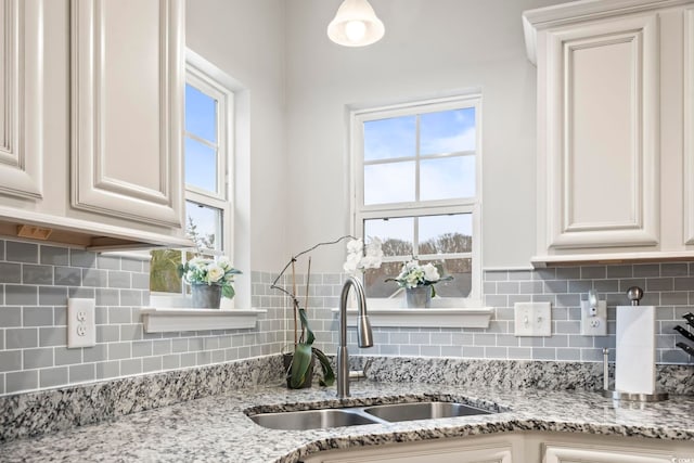 kitchen with light stone counters, sink, backsplash, and white cabinets