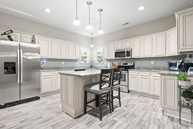 kitchen featuring light stone counters, white cabinetry, decorative light fixtures, appliances with stainless steel finishes, and a kitchen island