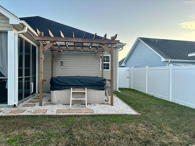 back house at dusk with a hot tub, a yard, and a pergola