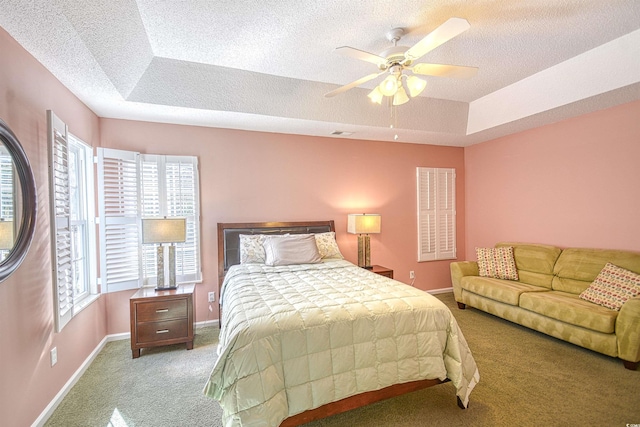 carpeted bedroom featuring a tray ceiling, ceiling fan, and a textured ceiling