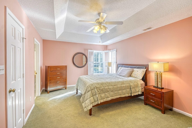 bedroom with a textured ceiling, ceiling fan, light carpet, and a tray ceiling