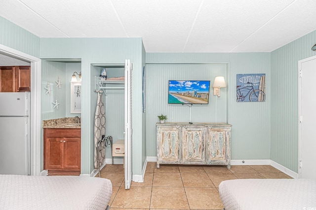 bedroom featuring light tile patterned flooring, a sink, freestanding refrigerator, and baseboards