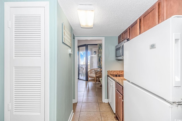 kitchen with a textured ceiling, light tile patterned flooring, freestanding refrigerator, brown cabinets, and stainless steel microwave